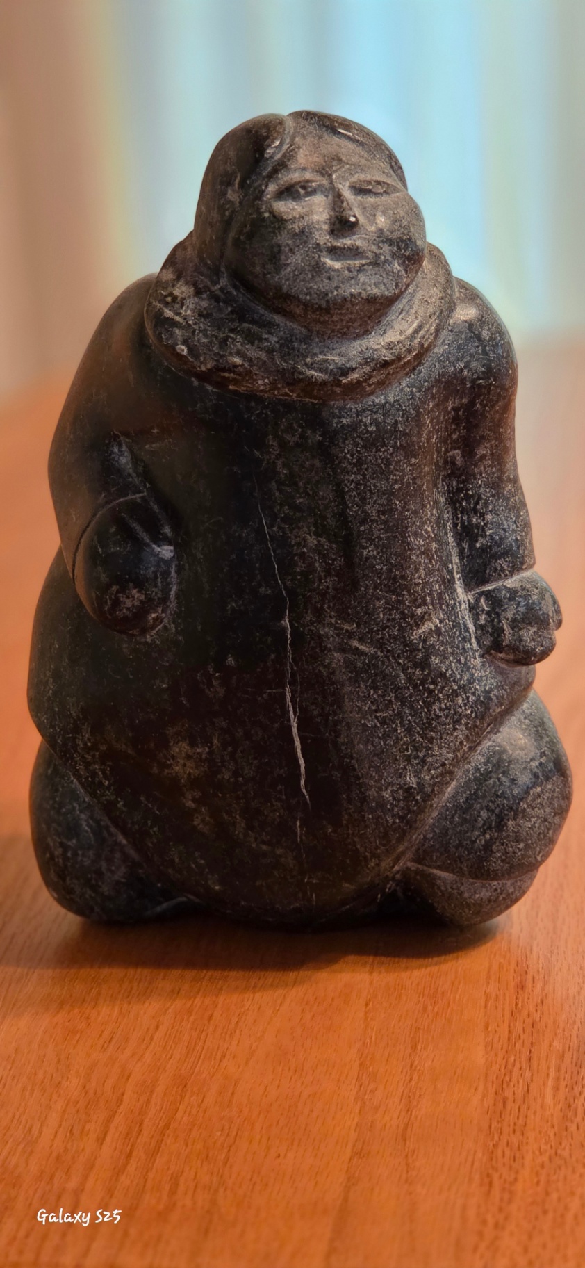 Inuit Soapstone Carving – Kneeling Figure in Traditional Parka Hand-carved stone sculpture depicting a kneeling Inuit figure wearing a traditional hooded parka, with detailed facial features and a naturalistic, weighted posture. - image 1 of 3