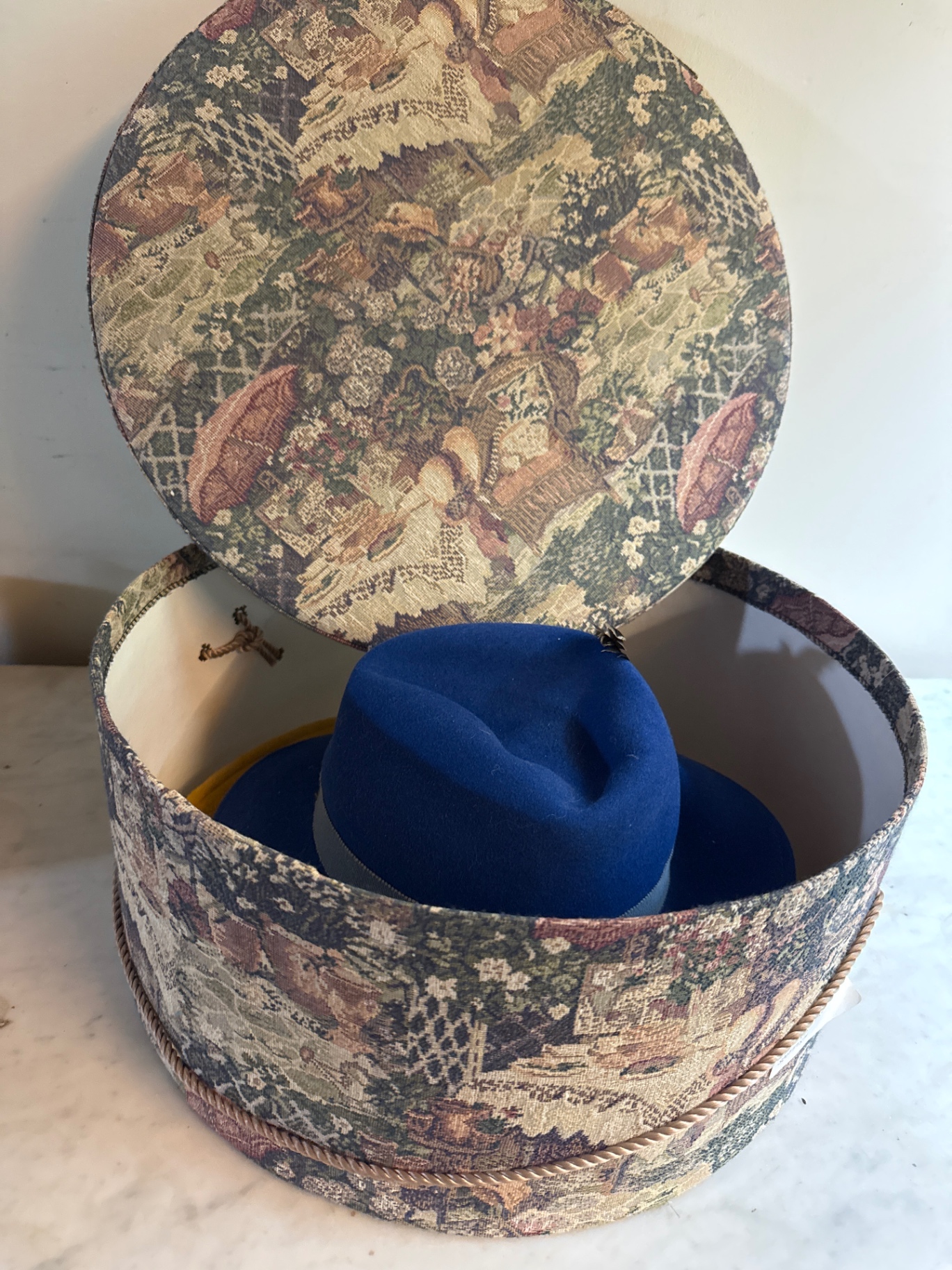 Round tapestry hatbox with blue and yellow hats - image 1 of 4