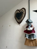 Heart-shaped wooden plaque with twine wreath and decorative fabric doll on a straw broom - thumbnail 1 of 5