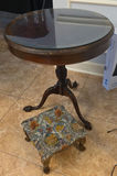 Round glass-top pedestal table with carved wooden base and floral upholstered ottoman - thumbnail 1 of 6