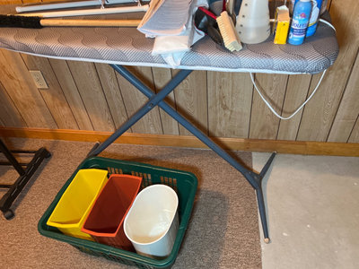 Ironing board setup with iron, cleaning supplies, and plastic storage bins - Image 1 of 6