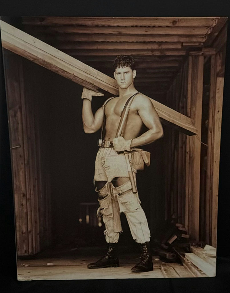 Man in distressed workwear with suspenders carrying a wooden beam - image 2 of 3