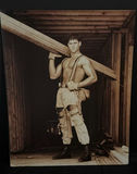 Man in distressed workwear with suspenders carrying a wooden beam - thumbnail 2 of 3