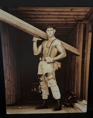 Man in distressed workwear with suspenders carrying a wooden beam - Image 1 of 3