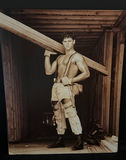 Man in distressed workwear with suspenders carrying a wooden beam - thumbnail 1 of 3