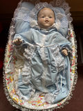 Porcelain baby doll in blue lace-trimmed gown in wicker cradle - thumbnail 1 of 6