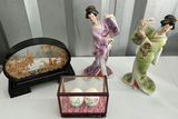 Geisha figurine, oval landscape plaque, and two painted eggs in glass display - thumbnail 1 of 6