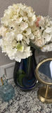 Hydrangea bouquet in blue glass vase with decorative bottles and brass mirror - thumbnail 4 of 5